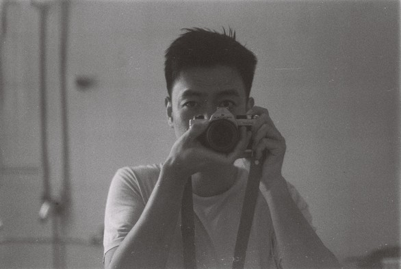 A black and white picture of a man holding a camera aiming at a mirror.
