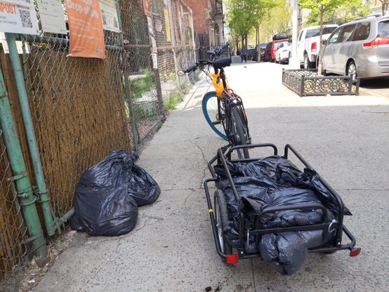 Ebike and bike trailer parts in front of Frank White memorial Garden with a load of three bags of coffee grounds. Two bags of coffee grounds are on the sidewalk from a prior delivery.