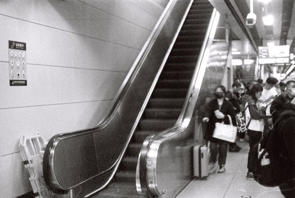 A black and white picture of people waiting for trains by the side of an escalator