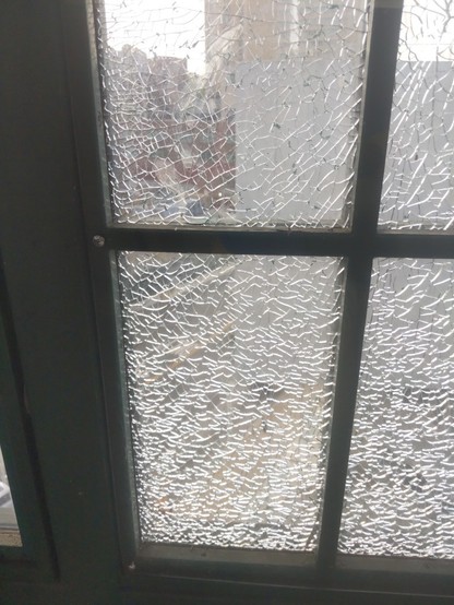 A window that is cracked and covered over with a sheet of plexiglass attached with some screws.