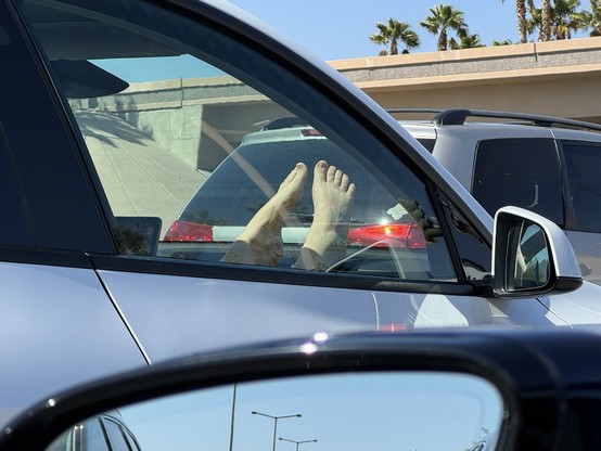 A woman’s bare feet are up on the passenger-side dashboard of a Tesla. 
