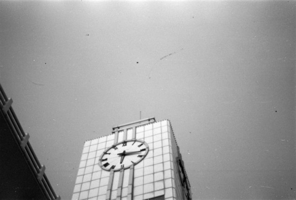 A black and white image of a portion of a clock tower against the sky. The clock is reading a quarter past six.