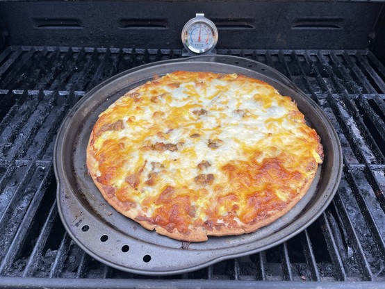 A picture of a cooked pizza on a pan on my outdoor grill with the cheese browned perfectly. I have an oven thermometer sitting on the grill that reads 350 F (was almost 400 F when I first opened the grill lid).