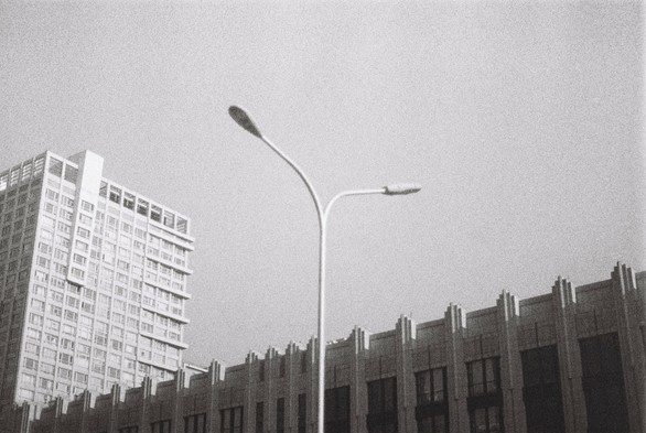 A black and white image of a street lamp set against two buildings and sky.