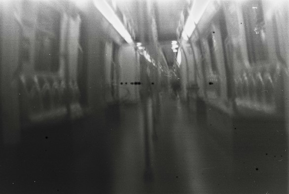 A black and white image of an empty subway train with light leak dots in the middle.