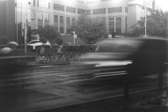 A black and white image of a car driving by, leaving the trace of a light strip.