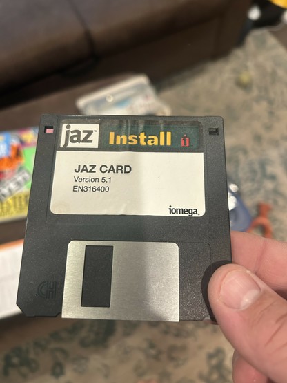 A hand holding a 3.5” black floppy disk with Iomega branding, saying Jaz Card version 5.1 en316400