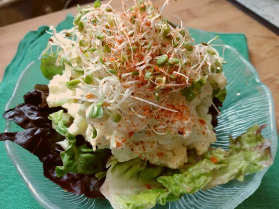 Egg and tofu salad on a bed of mixed lettuces, topped with mixed salad microgreen sprouts and a sprinkle of sriracha seasoning.