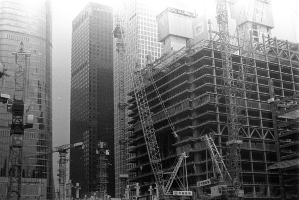 Black and white image of a construction site with cranes and unfinished buildings.