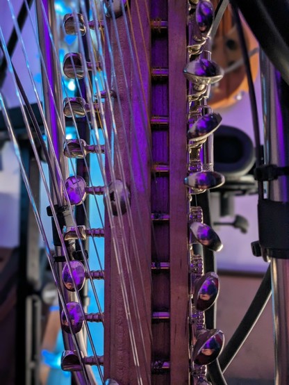 A closeup of the tuning bridge of THE GRAVIKORD, lots of nylon strings and metal tuning pegs, with purple light