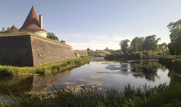 An external circular, red-roofed tower on the edges of the star fortress that houses kuressaare castle. Grass and a moat is in the foreground. Clear dusk sky. 