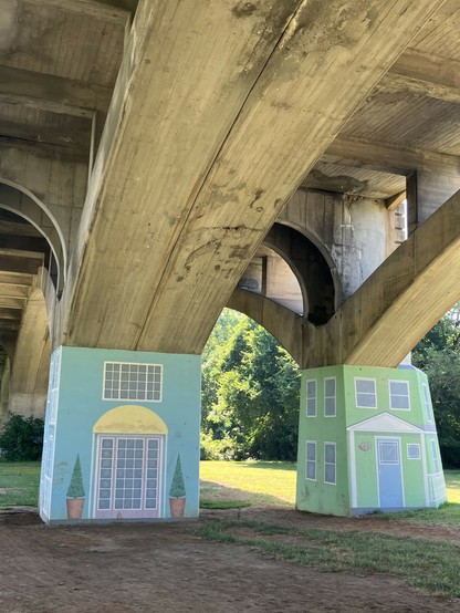 Concrete bridge supports painted to resemble building facades, with greenery in the background. No trolls visible. It’s too hot. 