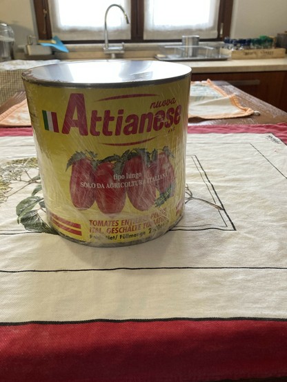 A huge can of Italian sauce tomatoes covered in plastic wrap. The can is on a kitchen island on a dish towel. 