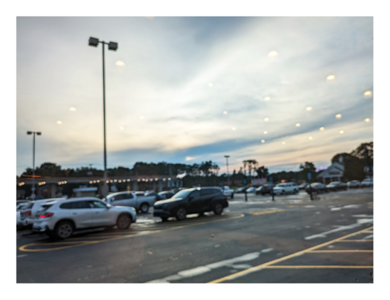 out of focus cars in a suburban supermarket parking lot at sunset. the sky features about 20 small white objects in a grid. a reflection of interior store lights on the window the scene is photographed through.