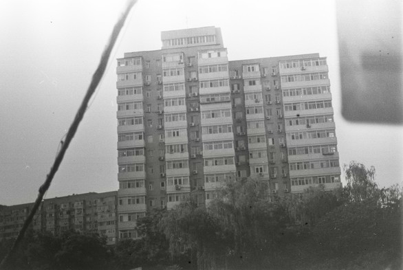 A black and white image of a power cable stretching in front of a residential building all the way next to a road sign.