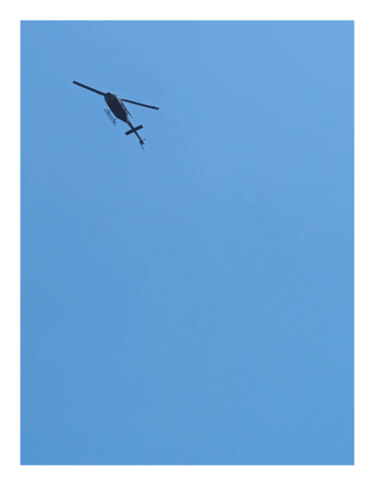 a black helicopter from below in a clear part of sky.