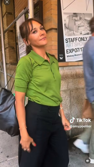 TikTok video with Rashida Jones doing a small dance in the middle of the frame and a random person walking past behind her, exiting the frame to the right 