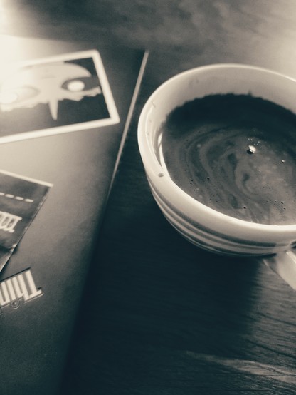 Black and white photo of a cup of coffee and part of an old thinkpad with some stickers on it.