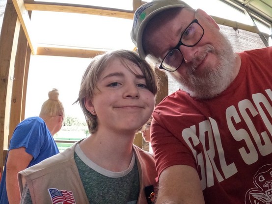 Picture of a Girl Scout with short blonde hair posing with and older man in a red GS shirt. 