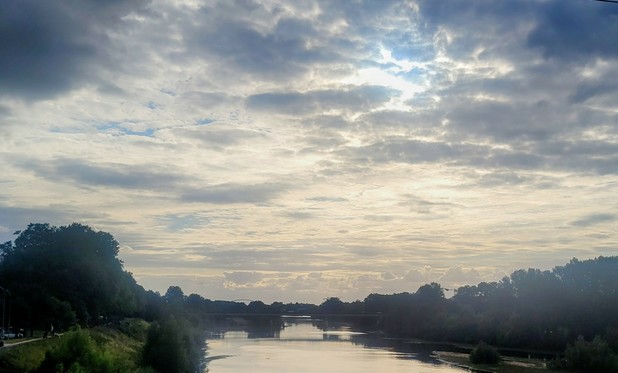 A view looking towards the west, in early evening, of a broad river, with a sky full of clouds. 