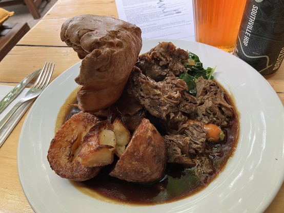 A large plate of moist falling-apart chunks and shreds of lamb shoulder, seriously roasted potatoes, Yorkshire pudding, braised greens, red cabbage, carrot, and swede (rutabaga) purée, with a dark, liquid gravy.