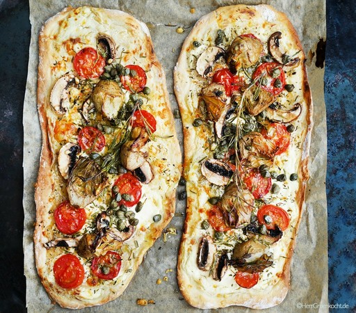 Zwei ovale Pizzen. Beide mit Tomaten, Pilzscheiben, Artischocken, Kapern und Rosmarin. Schön kross und dünn. Goldbraun an den Rändern.