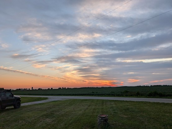 Sunrise over the corn field. Clear on the left, cloudy on the right. There's a line of silver edged clouds almost perfectly in the middle,on the left is purple, with very little clear, and on the right is a blue gradient with a stripe of orange on the horizon