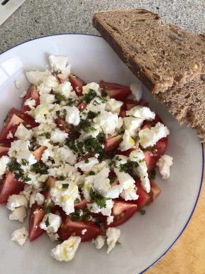 Tomaten, Feta, Kräuter und Olivenöl auf Teller, daneben Brot 