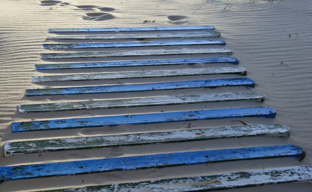 A wooden track across a sandy beach. The track is made of wooden slats painted, alternately, white and blue.