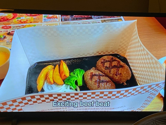 Still picture from a Japanese YouTube travel video on my TV.

A table in a famiresu (fast-casual chain restaurant). On it, a rectangular cast-iron plate with two small hambagu (Salisbury steak) patties, some potato wedges, sliced onion, and broccoli. Around the plate, a paper collar about 10cm high, which is supposed to stop the still-cooking meat from spattering over the table.

Subtitle at the bottom of the screen: 