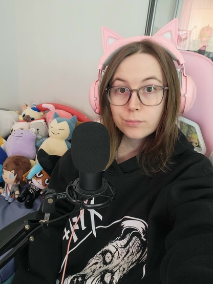 Selfie of Revy 
No makeup 
Wearing a Junji Ito hoodie
And thr background has many various plushies