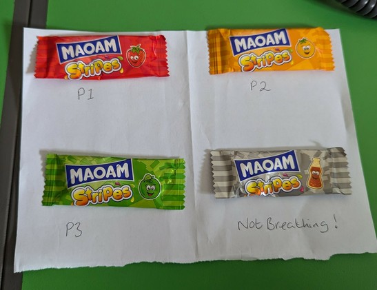 Four Maom sweets laid on a sheet of paper. The red sweet is labelled P1, the orange sweet is P2, the green one is P3 and the grey one is Not Breathing.