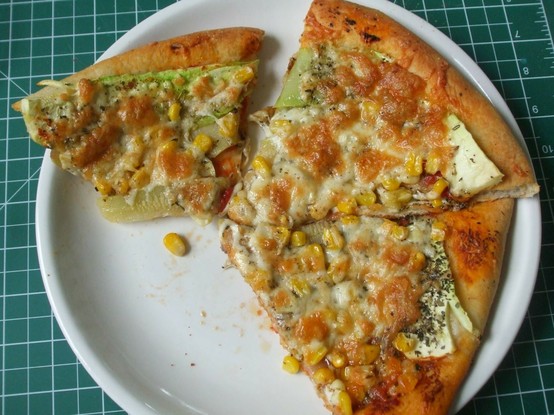 3 slices of corn and zucchini pizza topped with mozzarella on a white plate. A few bites missing from one slice.