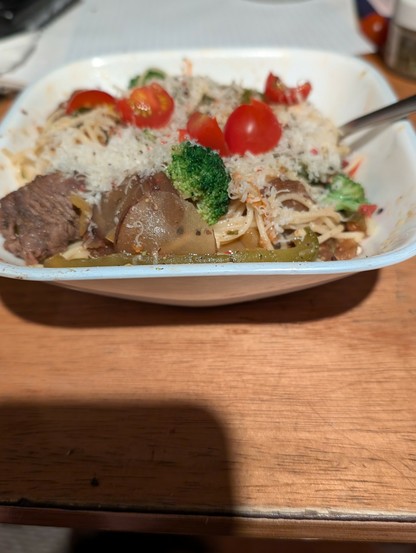 A bowl of pasta with steak, peppers, tomatoes and fresh Parmesan.