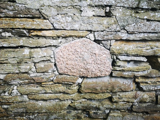 A flaggy sandstone wall in Stromness has within it just the one piece of roughly 5-sided pink granite. Other walls in the town are made from a mixture of flag and random shaped blocks of stone. This looks like the builder decided to make it a feature. 