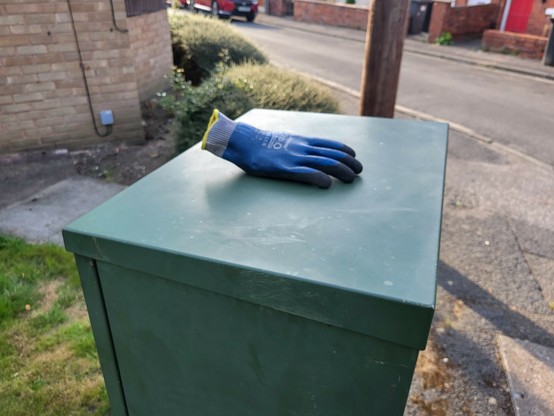Blue pvc glove on a green street furniture box. Grass and tarmack below.