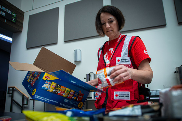 A woman in a Red Cross vest stocks snacks in an evacuation center