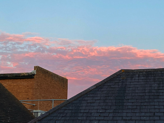 Sunset over Windsor. A band of pink clouds, seen over rooftops, against a blue sky.