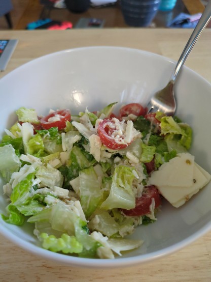 A bowl containing chopped up romaine lettuce, cut cherry tomatoes, shredded chicken breast, and shaved Parmesan cheese.