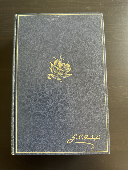 Big, dark blue book with a golden flower drawn on the cover, a small child sitting in the flower. In the lower right corner of the cover is the signature of H.C. Andersen also in gold. No other text on the cover.