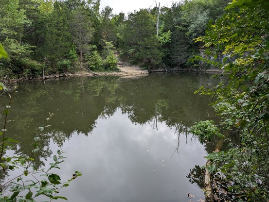 An abandoned quarry at Fallsville wildlife area near Hillsboro Ohio USA. Very dark green water reflects the trees that surround it. Grumpy skies above