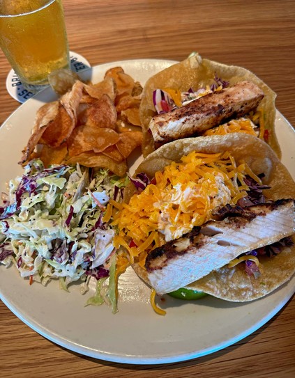 plate of swordfish tacos, cole slaw, and potato chips. glass of beer next to plate