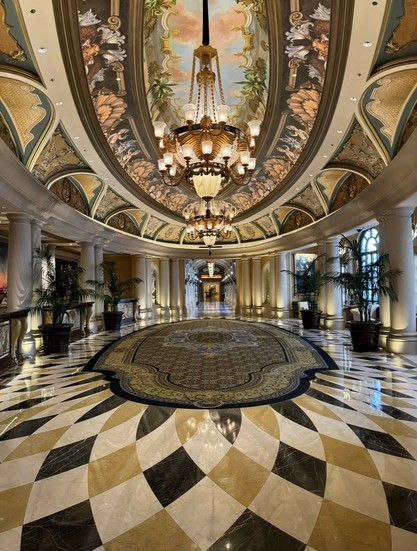 A lavish oval lobby with a domed ceiling decorated in Vegas’s version of Italian renaissance with patterned tile on the floor and painted ceilings. 