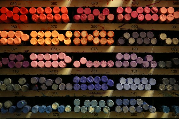 A wooden rack, filled with pastel chalks in graded colours. 