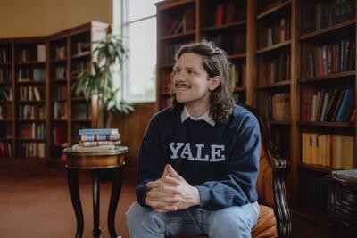 A college student in a Yale sweatshirt, seated in a library.