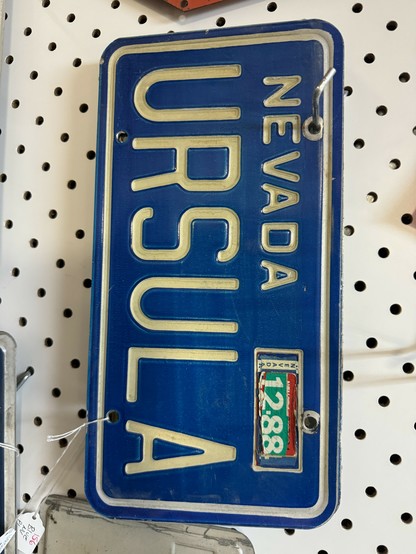 An old personalized NEVADA license plate reading URSULA is for sale in a vintage shop. 