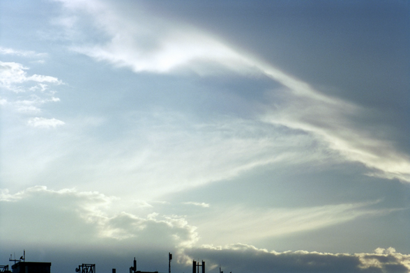 A glowing cloudscape fills the frame with bits of rooftop elements, antennae, cell transmitters, and the like, line the bottom end. 