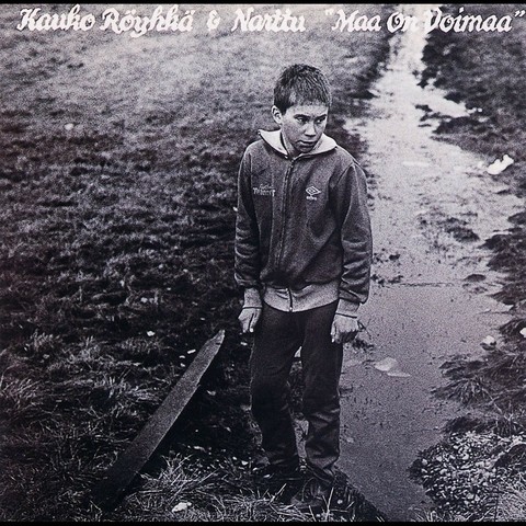 A teenage boy is standing by a ditch (by a field (supposedly)). He’s is looking out of the picture frame, and seems slightly pissed off. He’s wearing an old-fashioned sweatsuit. There’s an iron bar by his feet. The band in question is Kauko Röyhkä & Narttu, and the name of the record is ”Maa on Voimaa” (”Earth Is Power”).