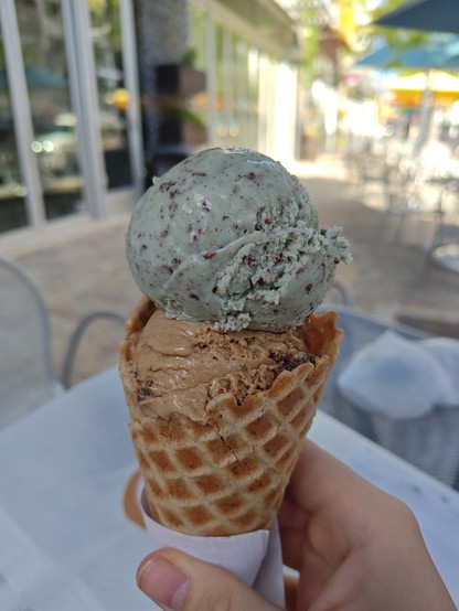 A waffle cone holding two scoops of ice cream: the bottom is coffee chip, and the top is mint chip.