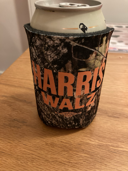 Beer koozie that is camoflage neoprene with Harris Walz in bright orange. 